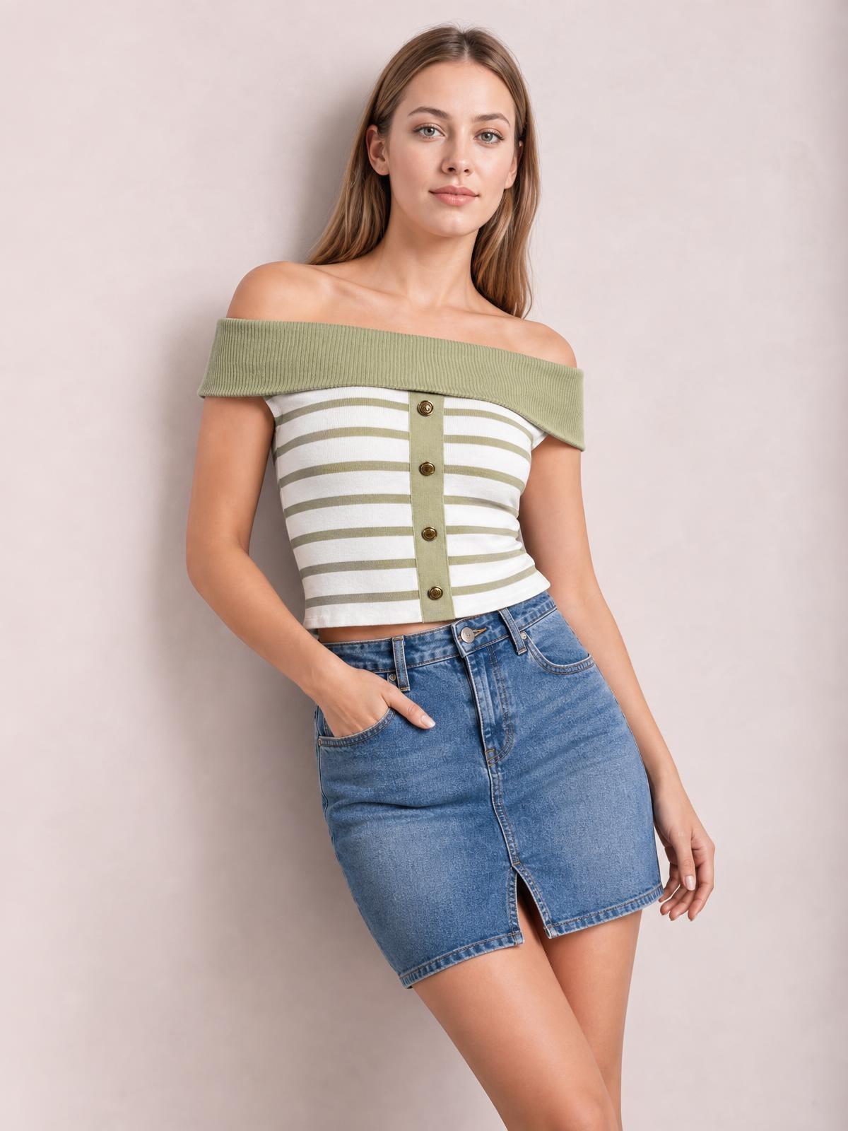 Model poses with one hand in her pocket wearing a fitted olive green and white striped knit top with an off-shoulder neckline and decorative front buttons.