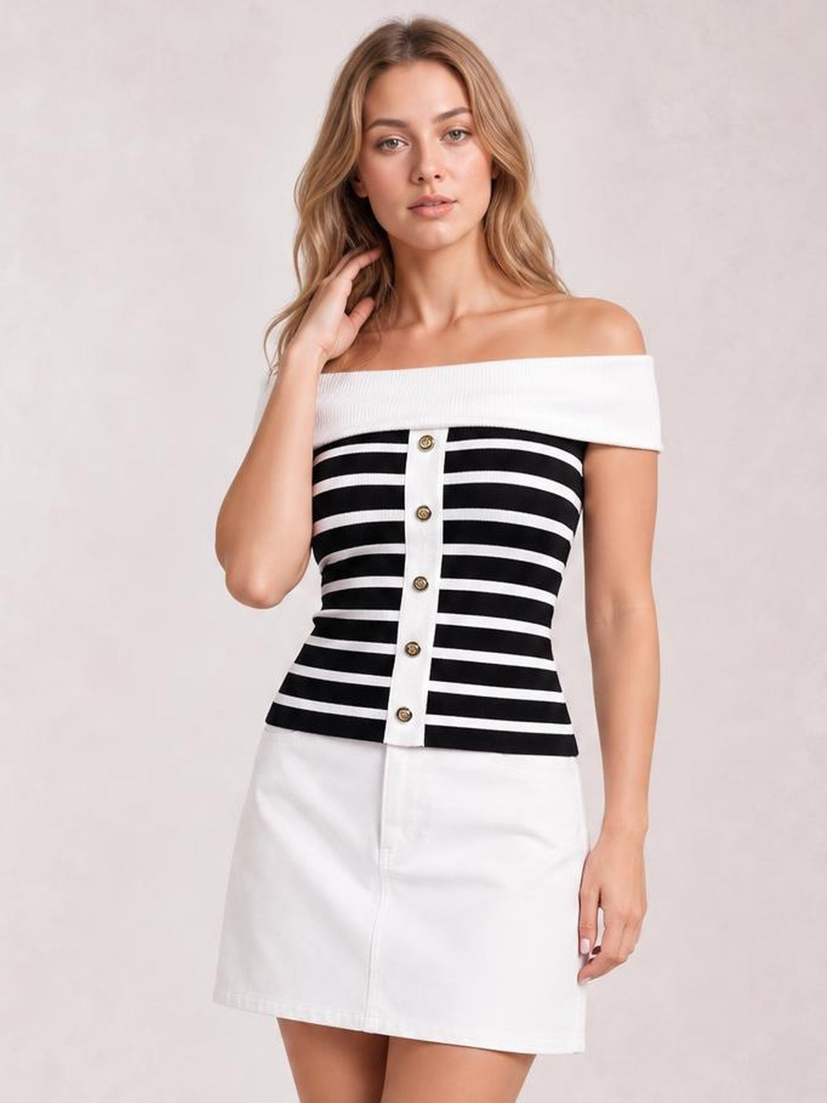 Model poses with one hand in her hair wearing a black-and-white striped off-shoulder knit top with decorative button placket and fitted silhouette.