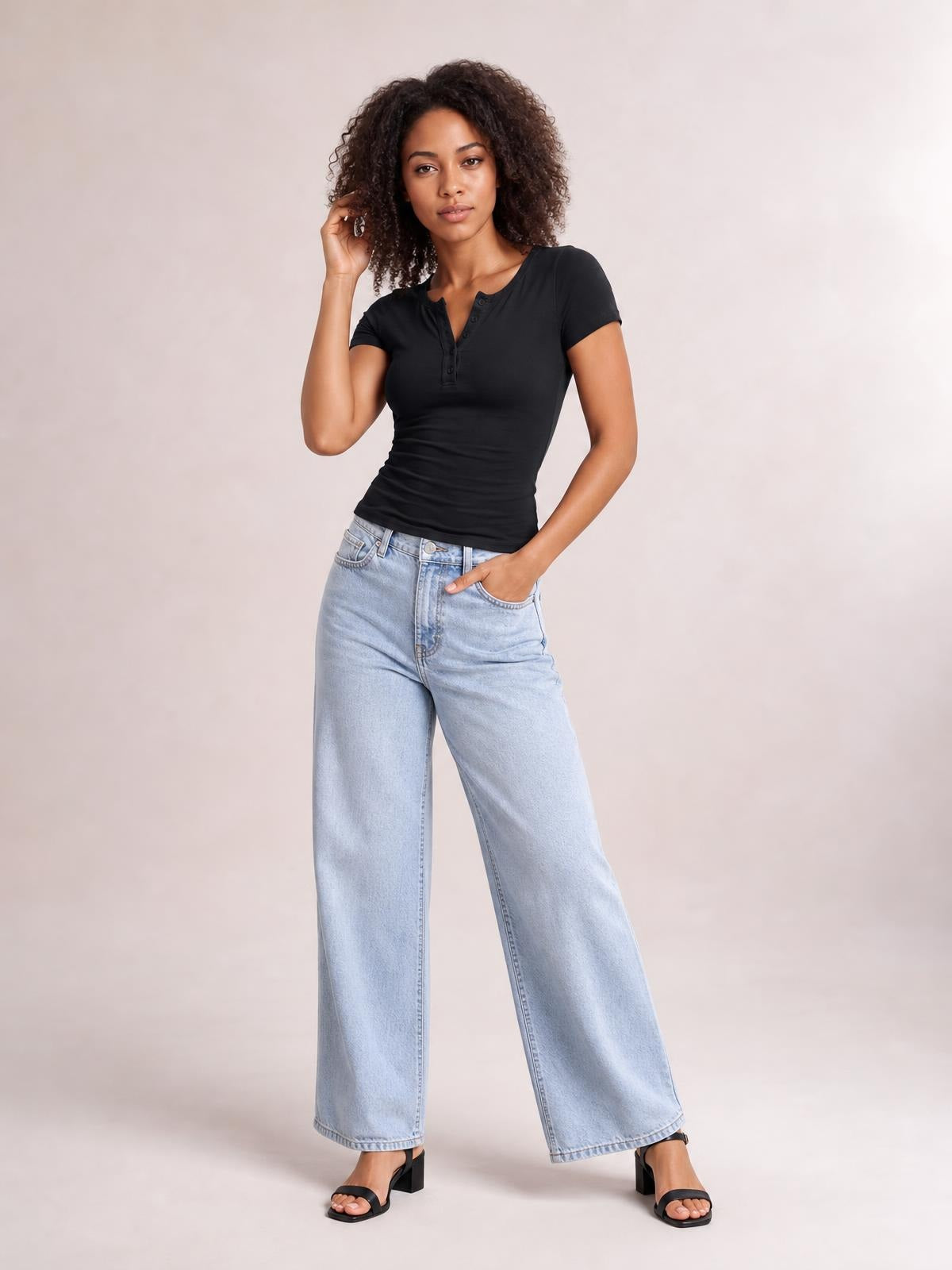 Model poses in a fitted black short sleeve T-shirt with buttoned neckline and stretch silhouette, paired with light-wash wide-leg jeans.