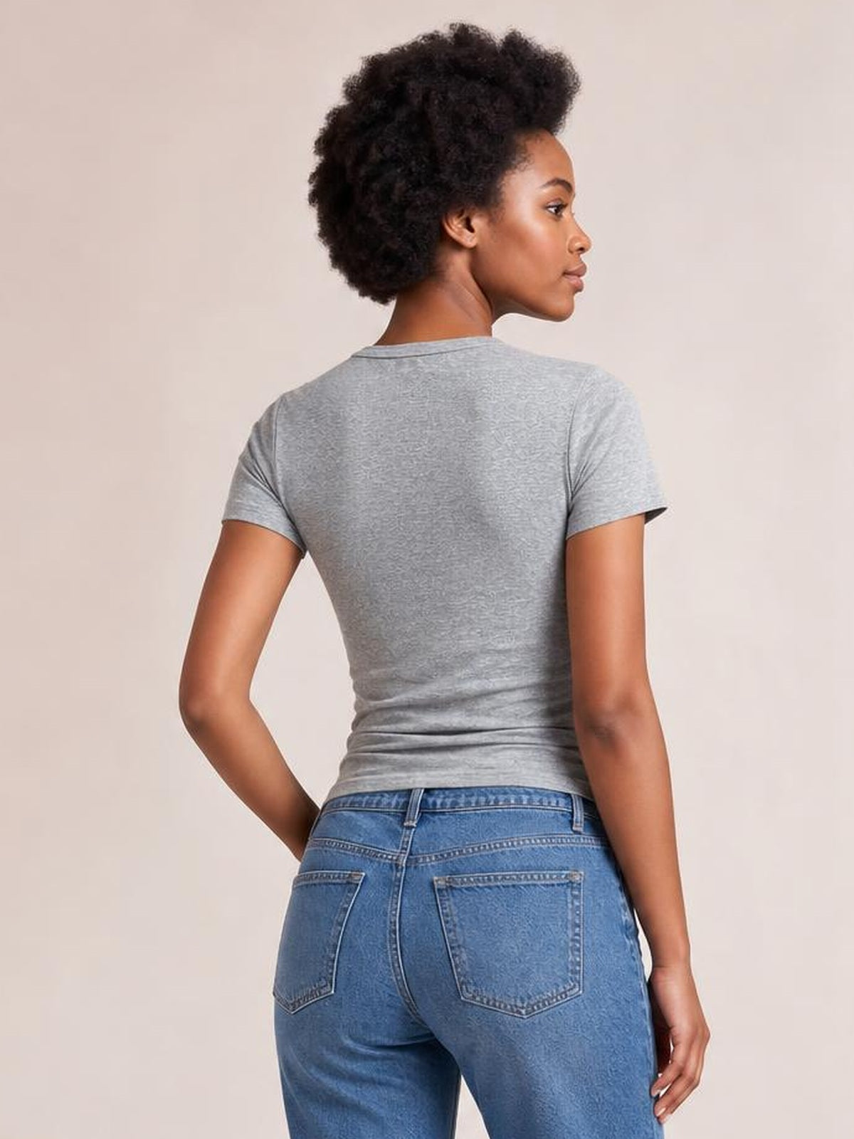 A model turns to show the back of a gray short-sleeve T-shirt with a fitted, stretchy silhouette, crew neckline, and opaque construction.