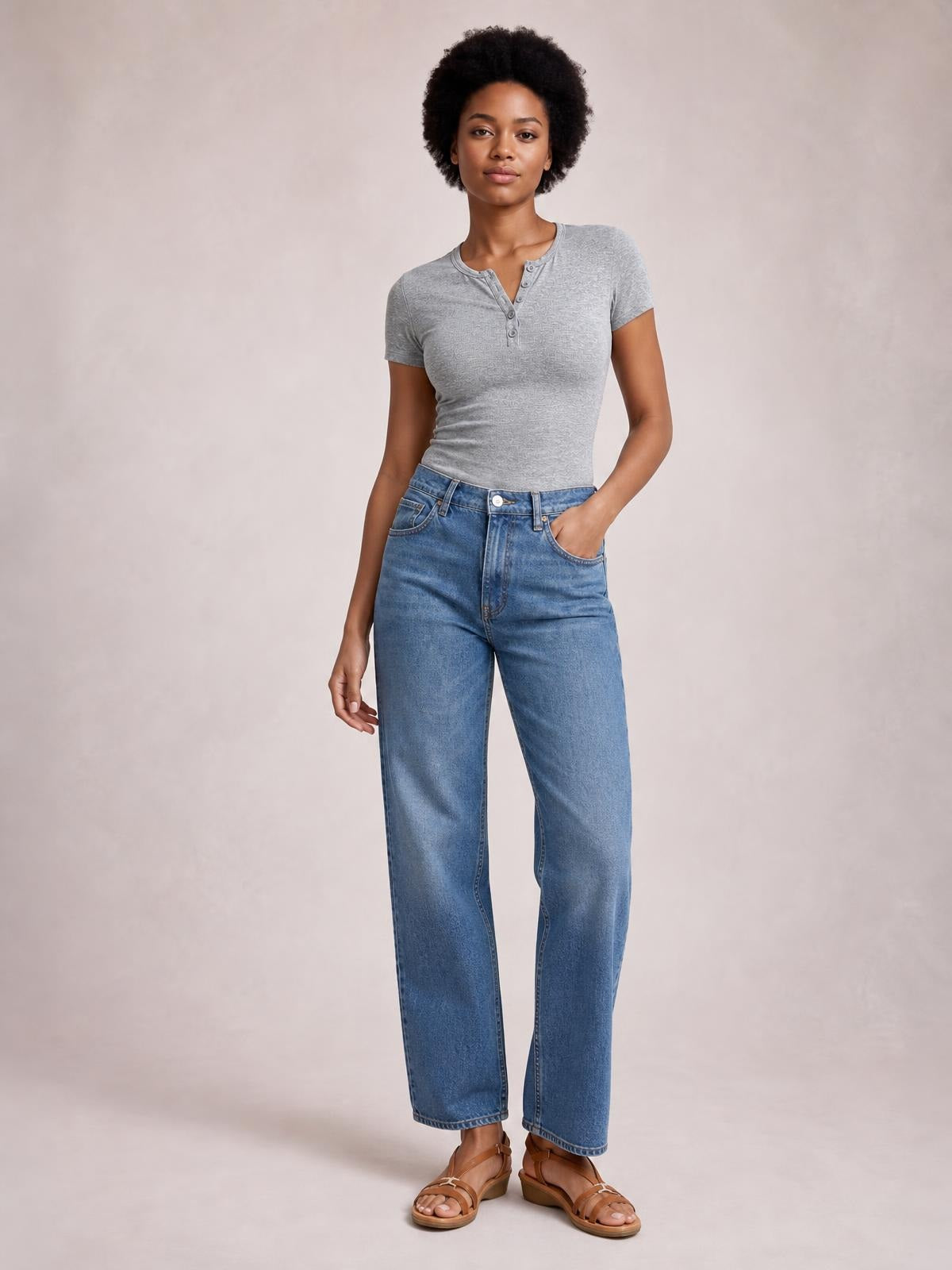 Model poses in a fitted gray short-sleeve T-shirt with a buttoned split neckline and subtle gathered construction, paired with relaxed straight-leg jeans.