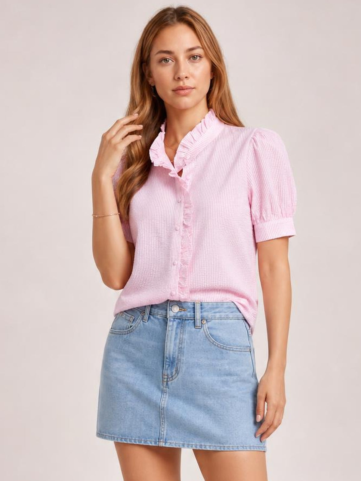 A model poses in a pink striped button-down shirt with short puff sleeves, a ruffled collar and front placket, and a relaxed silhouette.