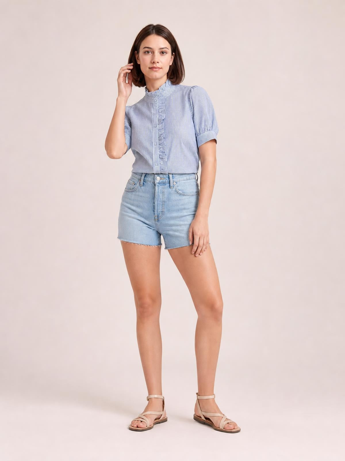 Model poses in a light blue striped button-down shirt with short puff sleeves, a ruffled front placket, and a tucked-in silhouette.