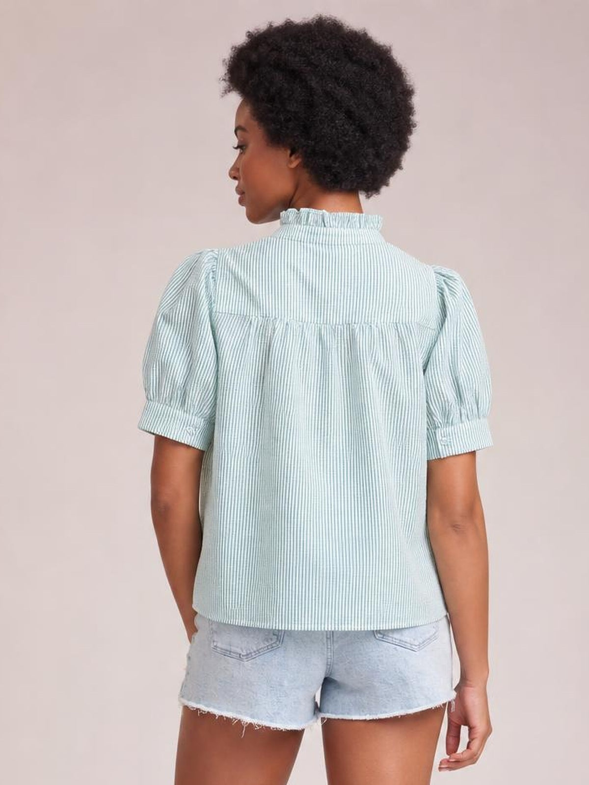 Model shown from behind wearing a pale blue and white striped button-down shirt with short puff sleeves, a gathered back yoke, and relaxed silhouette.