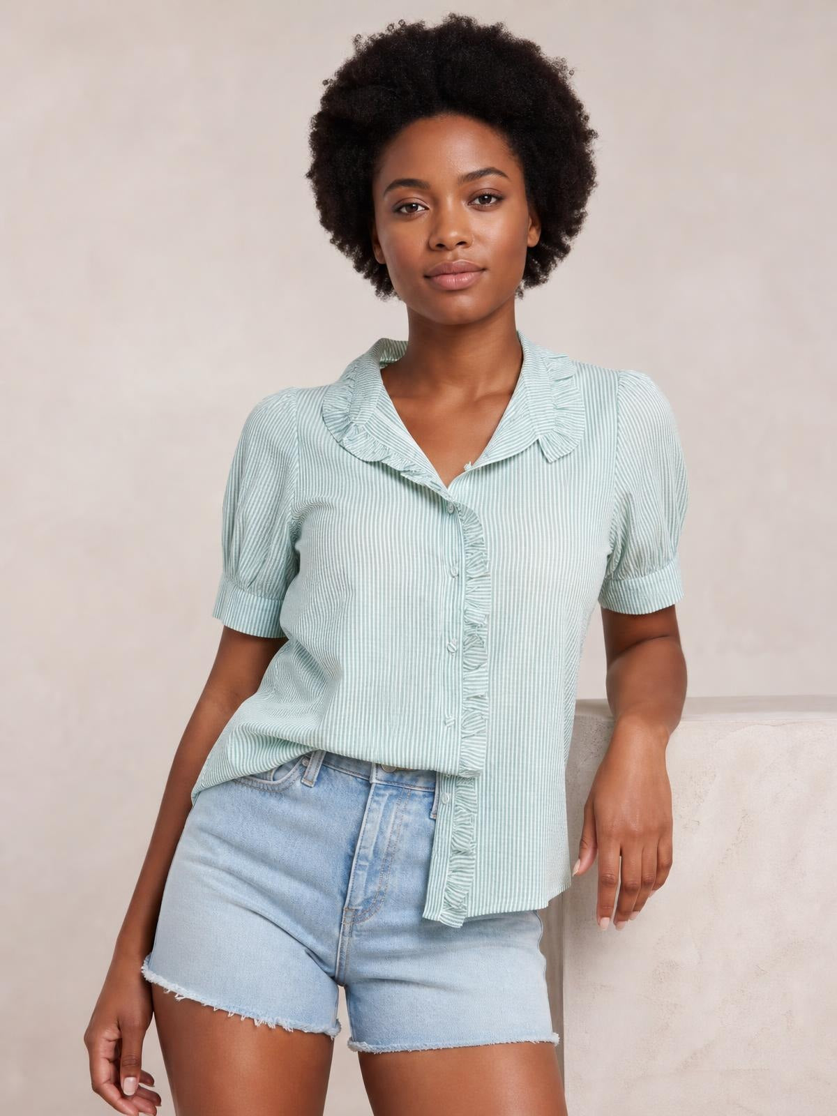 Model poses in a mint green striped short sleeve button-down shirt with a ruffled collar, button placket, and relaxed silhouette.
