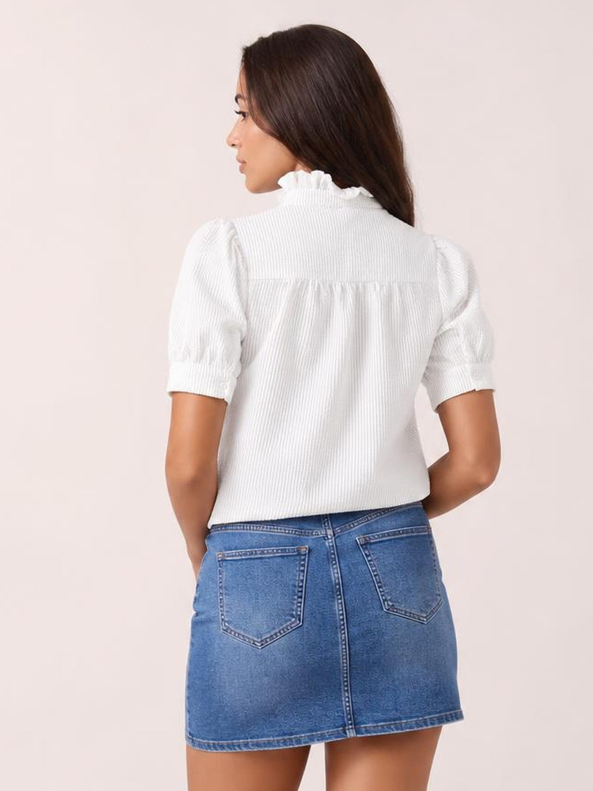 Model turned away wears a white striped short-sleeve shirt with a ruffled collar, gathered back yoke, and relaxed silhouette.