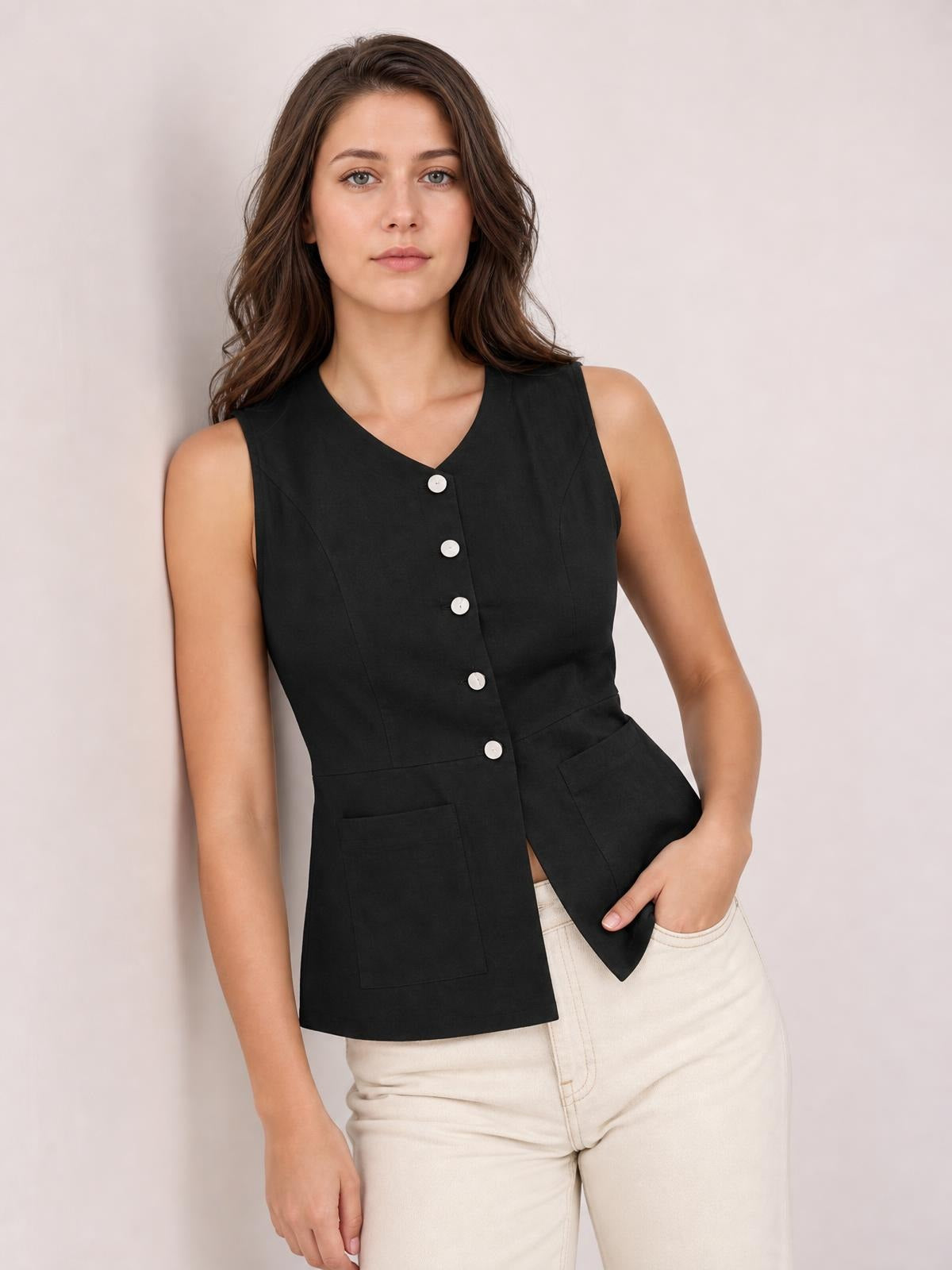 A model wears a black button-down V-neck sleeveless top with a fitted waist, front buttons, two patch pockets, and one hand in a pocket.