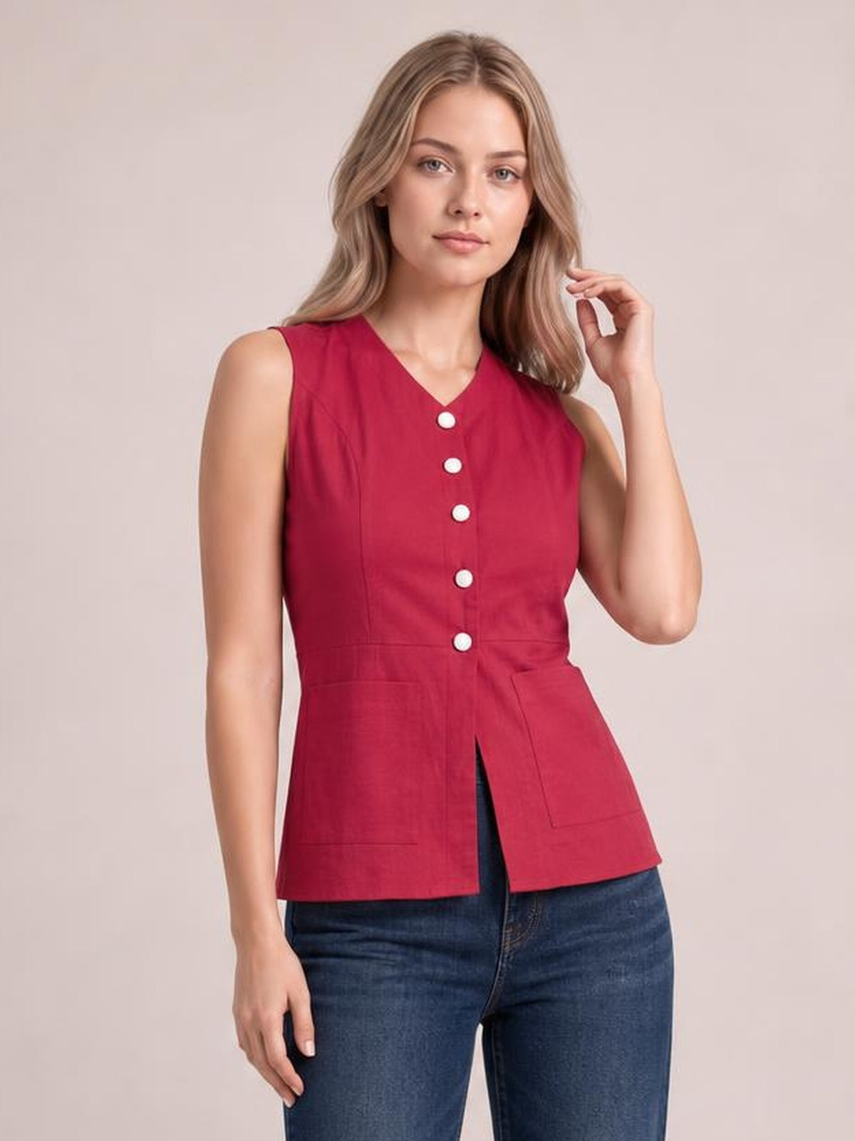 A model poses in a red sleeveless button-down V-neck top with a fitted waist, front buttons, structured seams, and large patch pockets.