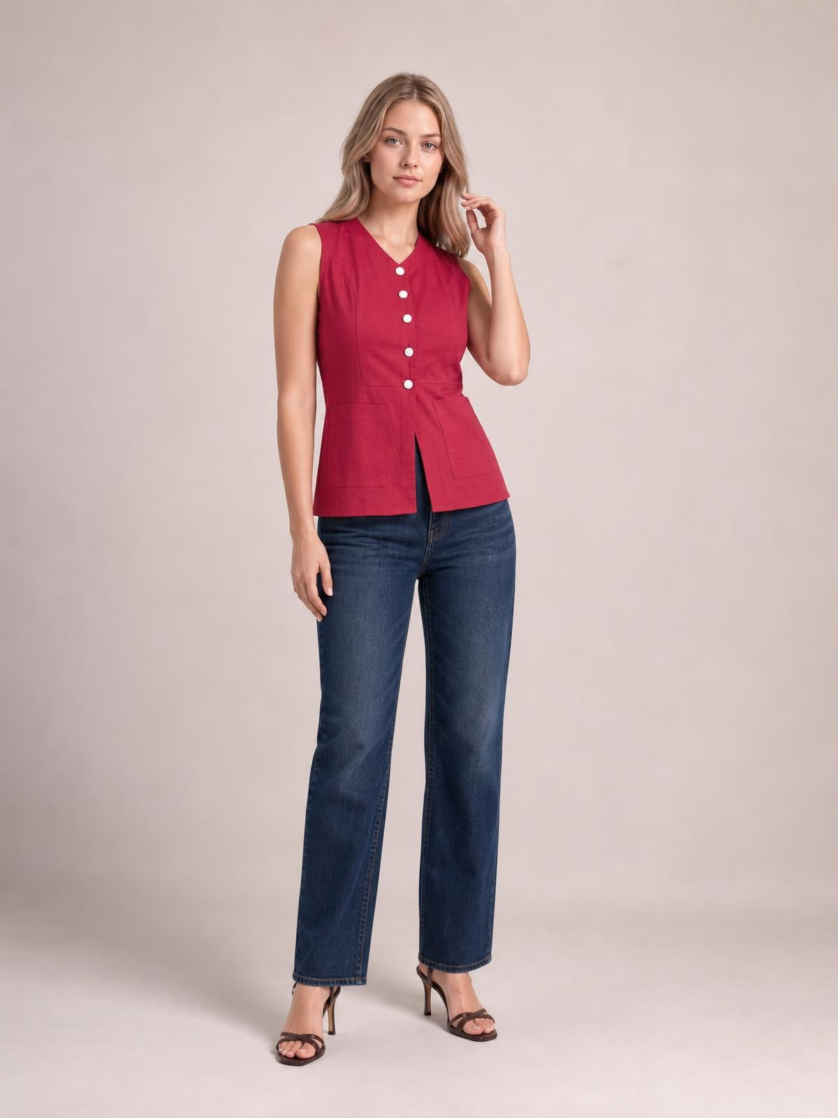 Model wearing a red sleeveless V-neck button-down top with white buttons, patch pockets, a structured waist, and a flared hem, posing in jeans.