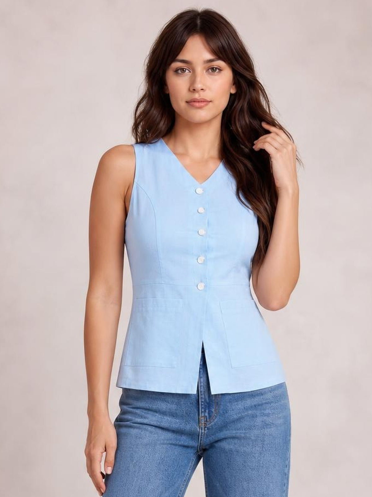 Model poses in a light blue sleeveless V-neck top with a button-down front, structured seams, fitted waist, and straight hem over jeans.