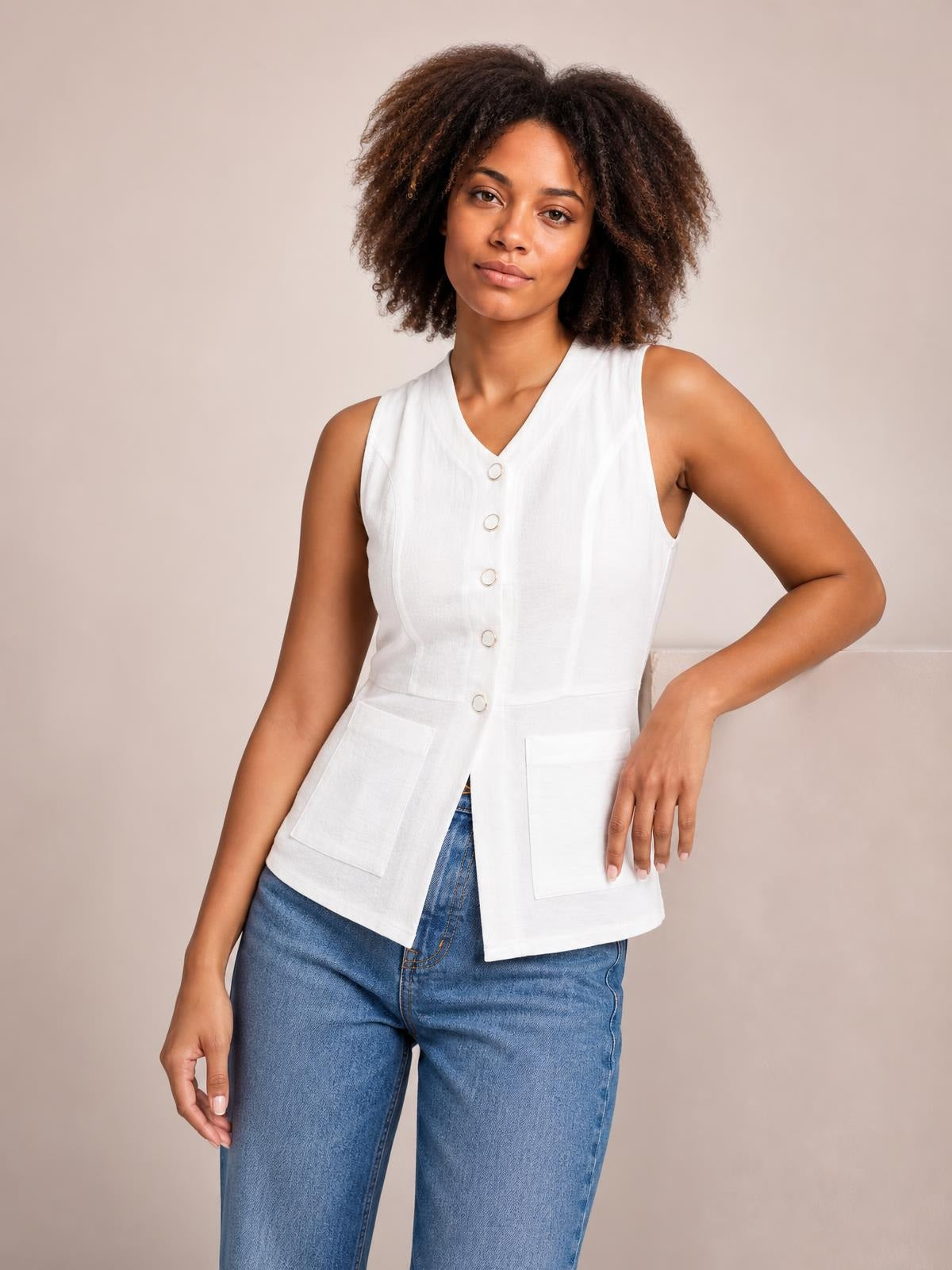 Model poses in a white button-down V-neck sleeveless top with a fitted silhouette, front buttons, and two large patch pockets.