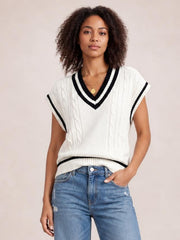 Model wearing a white cable-knit V-neck sweater vest with black striped ribbed trim, sleeveless silhouette, and a relaxed hem over jeans.