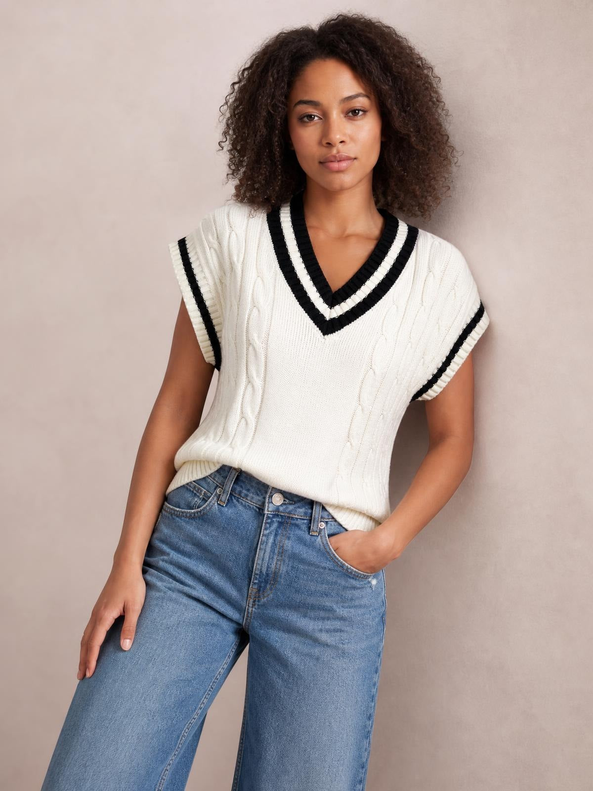 Model wears a white cable-knit V-neck sweater vest with black-and-white striped ribbed trim, sleeveless construction, and a relaxed silhouette.