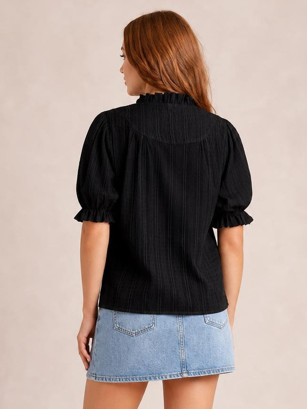 Model shown from behind wearing a black short sleeve blouse with a relaxed silhouette, ruched frill cuffs, and a gathered ruffle neckline.