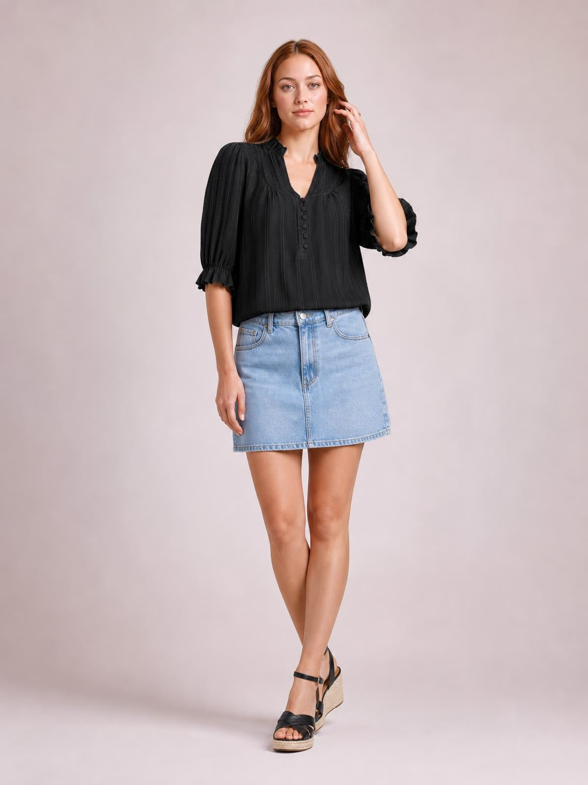 Model wears a black frill notched short sleeve blouse with a button front, ruched texture, puffed sleeves, frilled cuffs, and a relaxed silhouette.