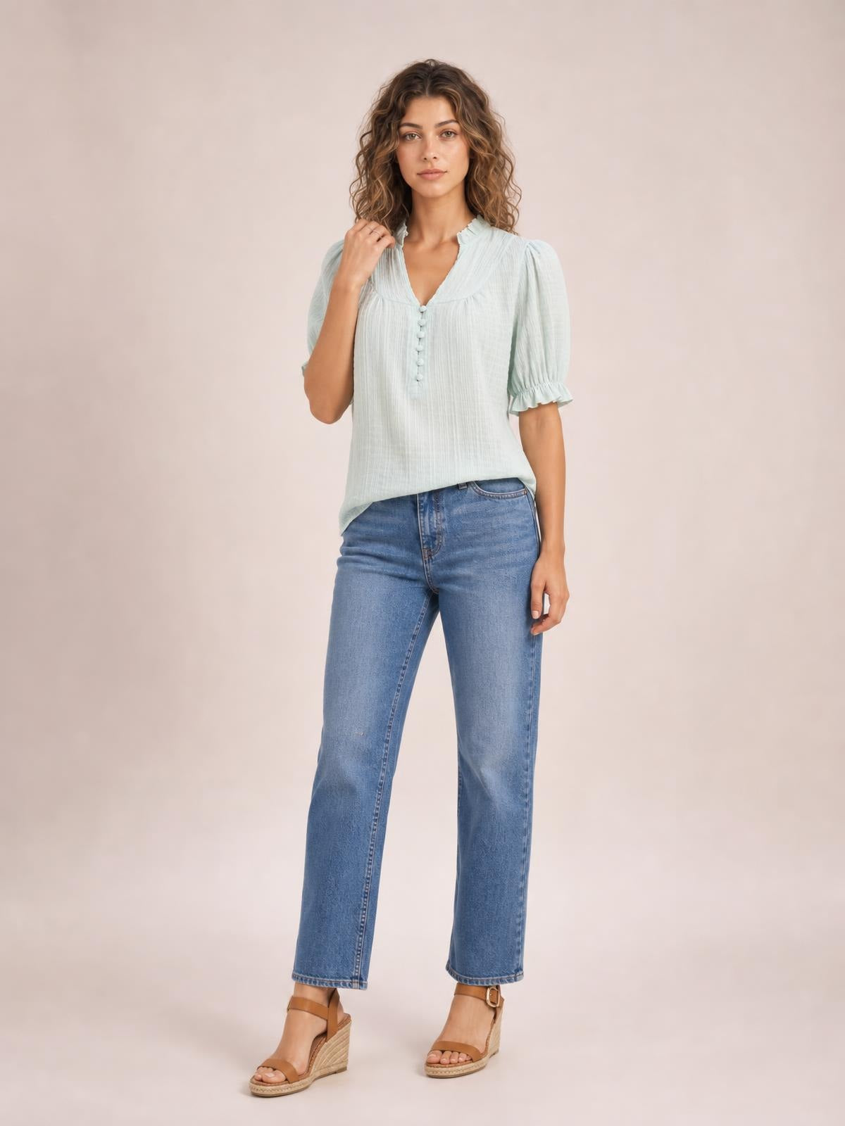 Model wears a pale mint frill notched short sleeve blouse with ruched texture, button front, puffed sleeves, and a relaxed silhouette while standing with one hand raised.
