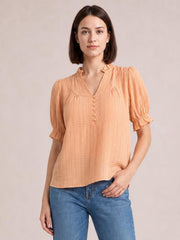 Model wearing a peach frill notched short sleeve blouse with ruched shoulders, puff sleeves, vertical texture, button front, and a relaxed straight silhouette.
