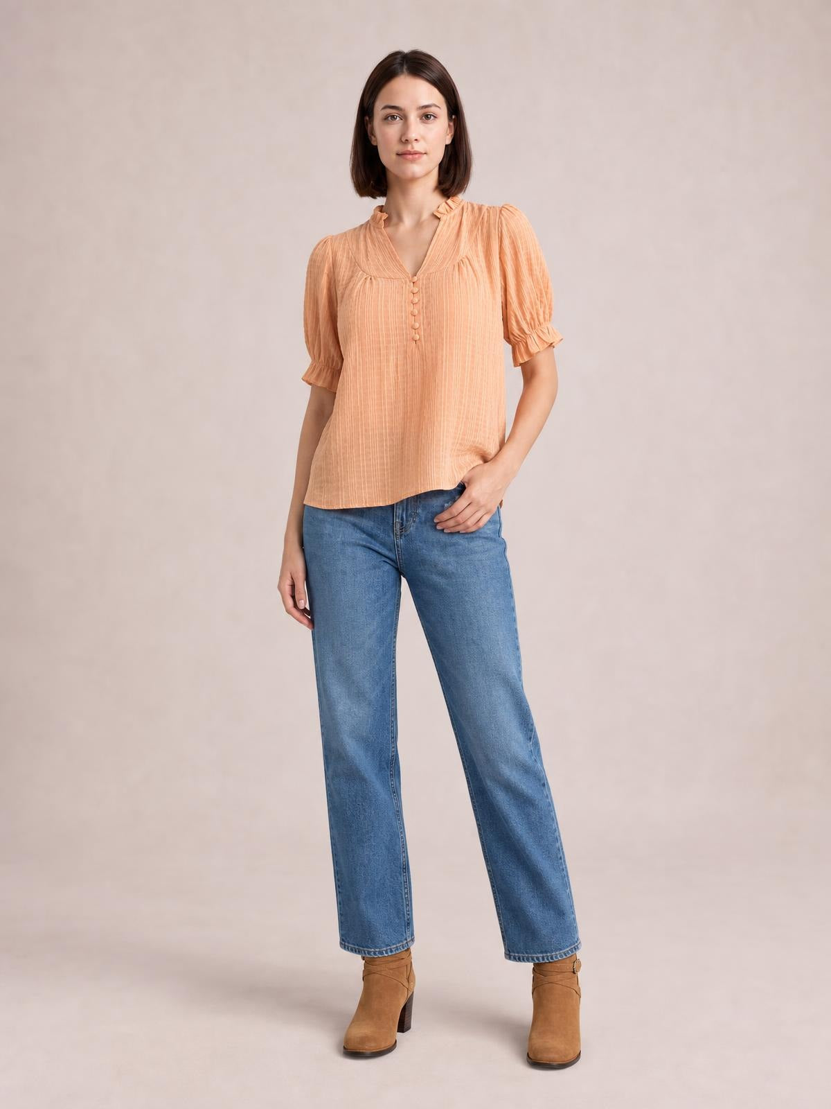 Model wears a peach frill notched short sleeve blouse with ruched texture, button front, puffed sleeves, ruffled cuffs, and a relaxed silhouette.
