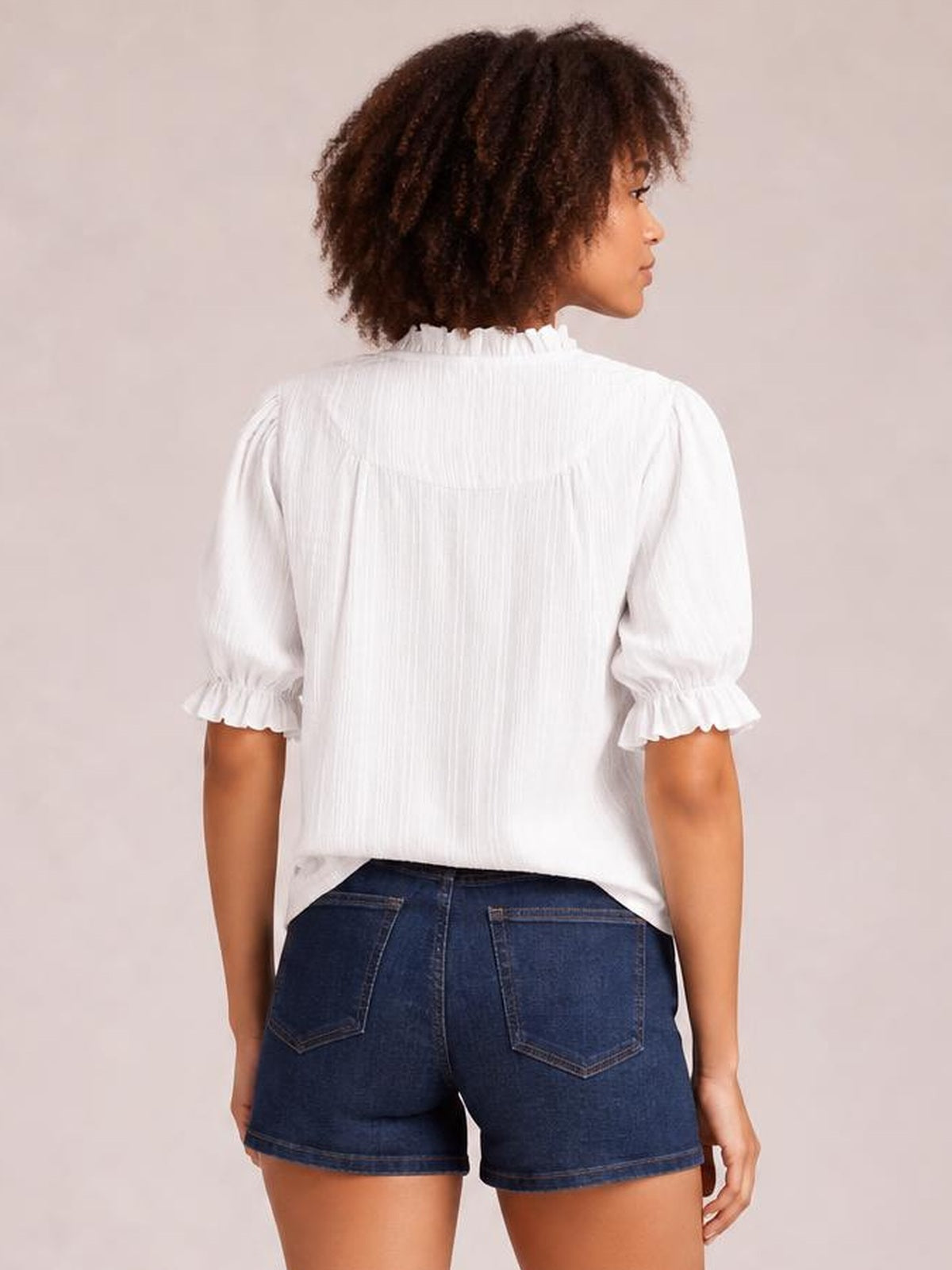 Model shown from behind wearing a white frill blouse with short puff sleeves, ruffled cuffs, a gathered neckline, and a relaxed straight silhouette.