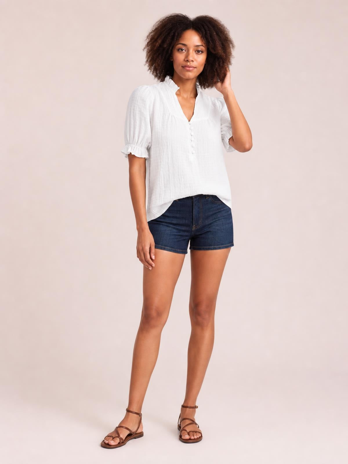 A model stands in a white frill notched blouse with a button front, ruched texture, short puff sleeves, and ruffled cuffs in a relaxed silhouette.