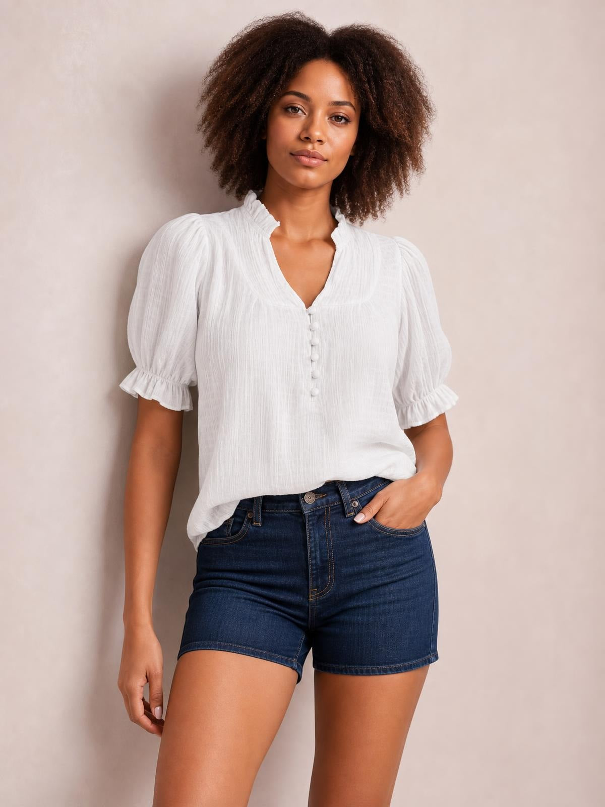 Model wearing a white frill notched short sleeve blouse with ruched texture, puffed sleeves, ruffled cuffs, button front, and a relaxed silhouette.