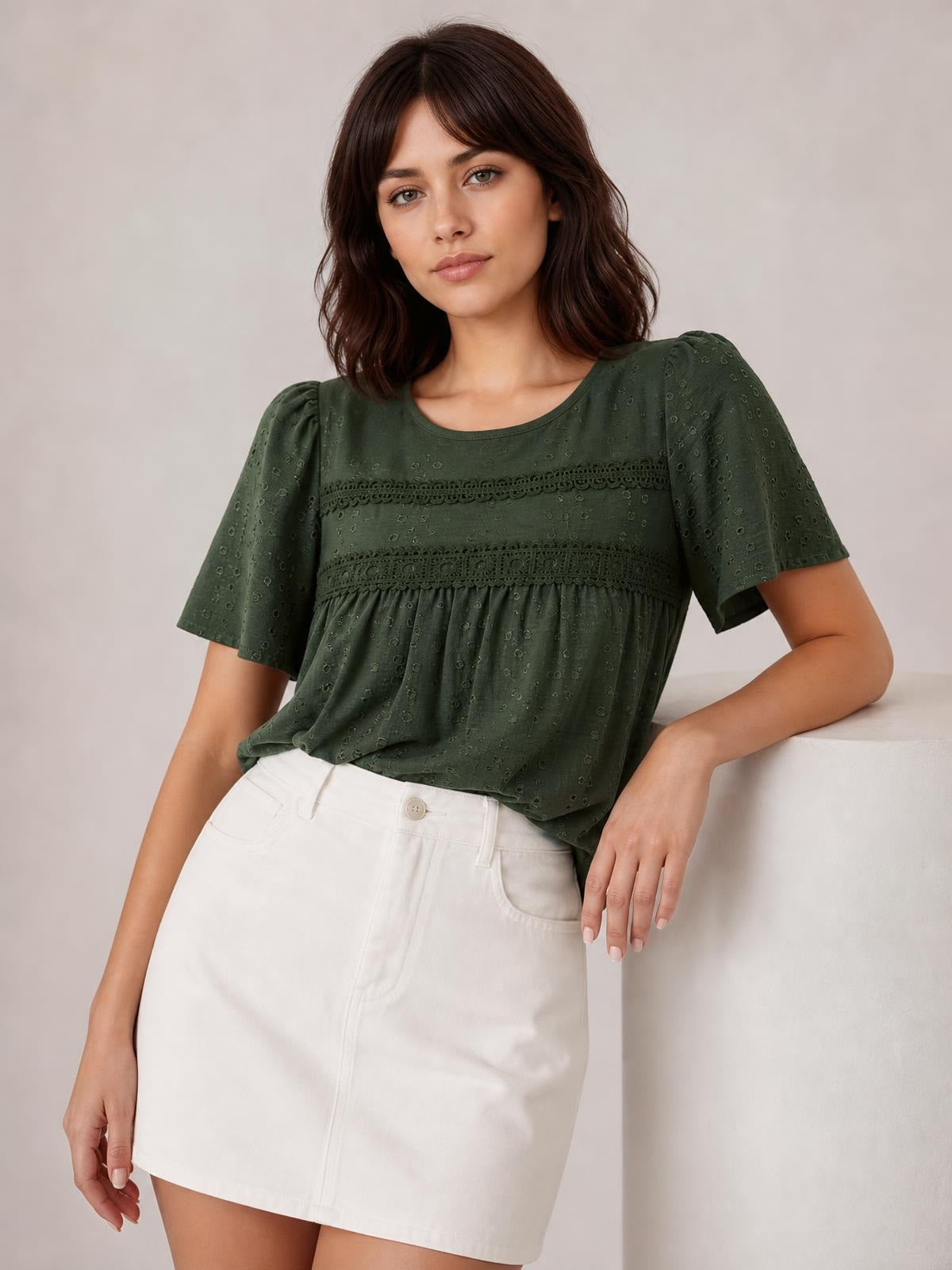 Model poses in an olive green round-neck short-sleeve blouse with lace detail, ruched seams, and a relaxed gathered silhouette.