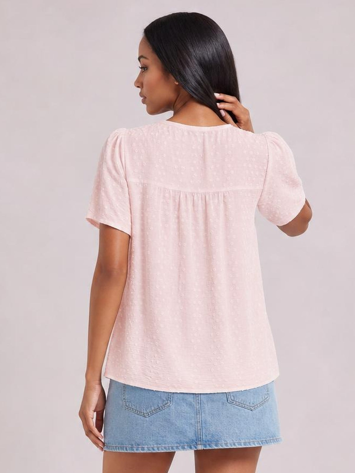 A model wears a pale pink lace-detail blouse with a round neck, short sleeves, gathered yoke, and relaxed straight silhouette while touching her hair.