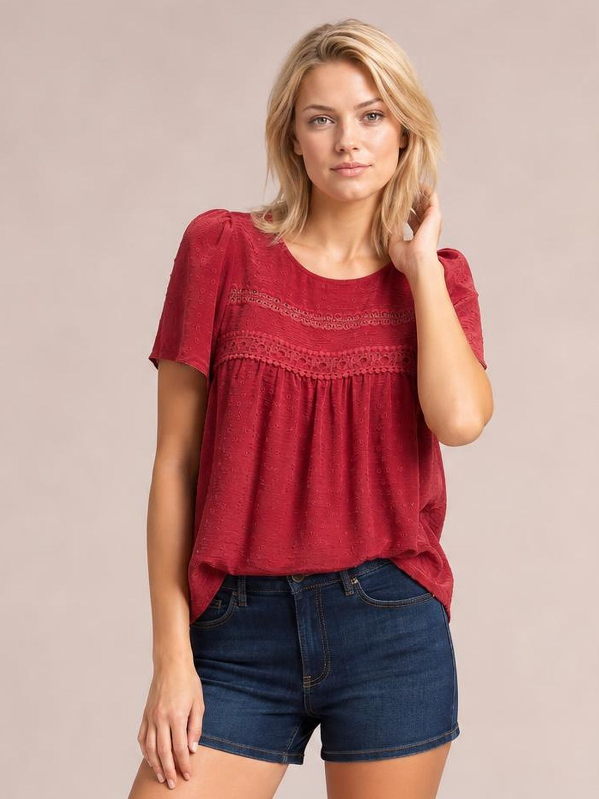 Model wearing a red lace detail round neck short sleeve blouse with ruched bands and a loose, flowy silhouette, posing with one hand in her hair.