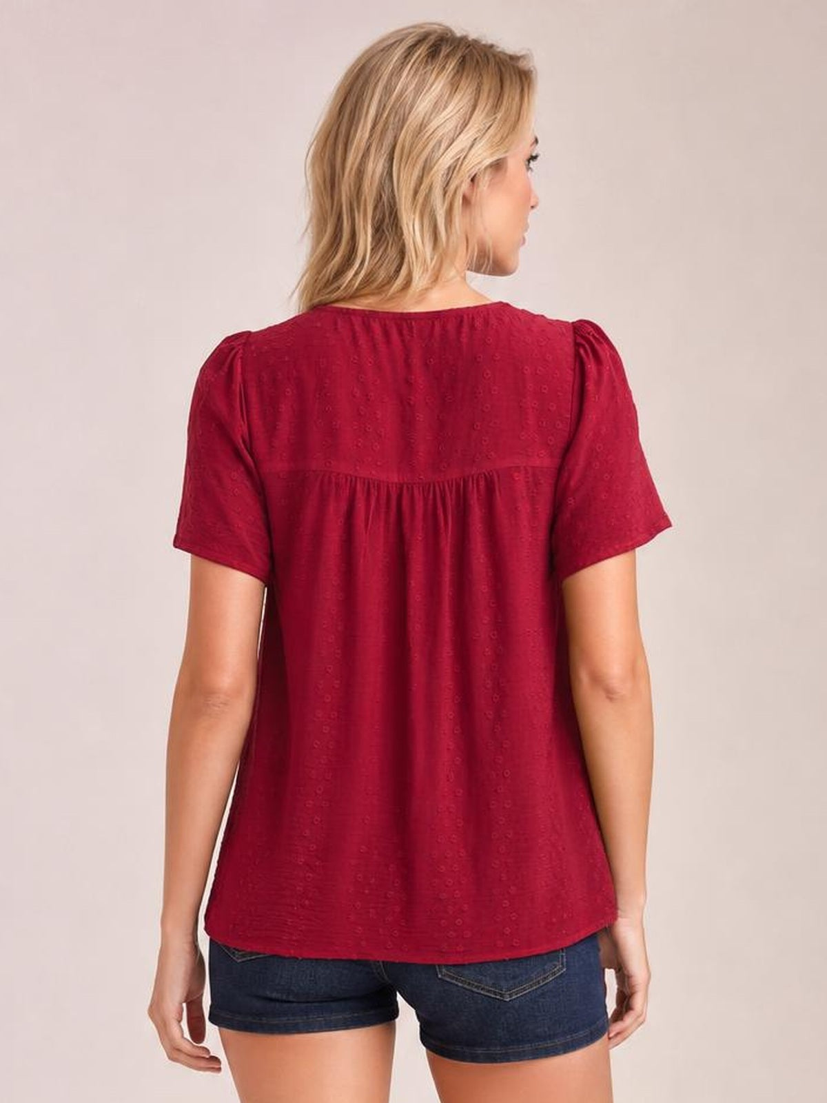 Model shown from behind wearing a burgundy lace-detail round-neck blouse with short sleeves, gathered yoke, ruched construction, and a relaxed silhouette.
