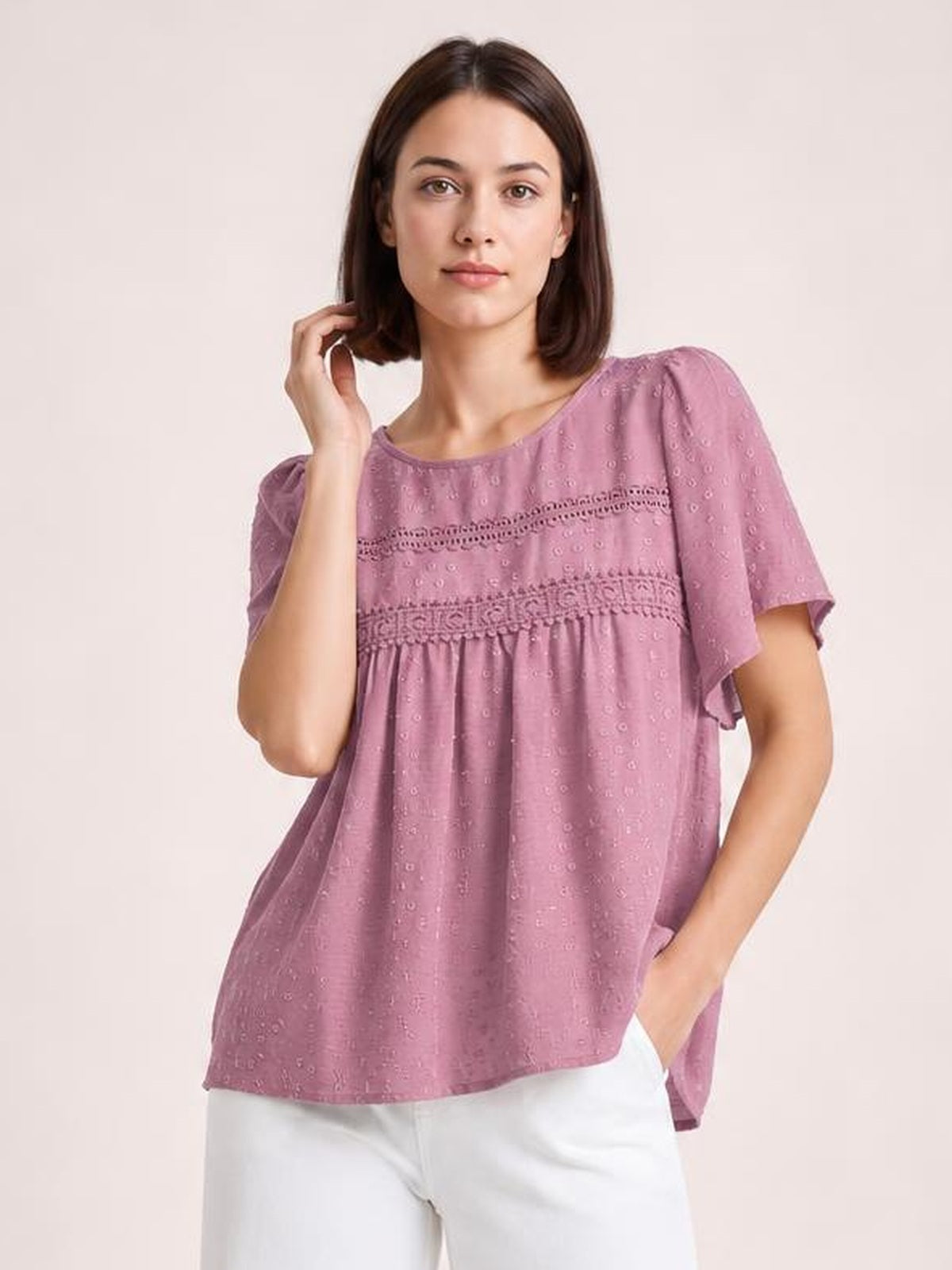 Model wearing a mauve lace detail round neck blouse with short flutter sleeves, ruched horizontal trim, and a relaxed, flowing silhouette.