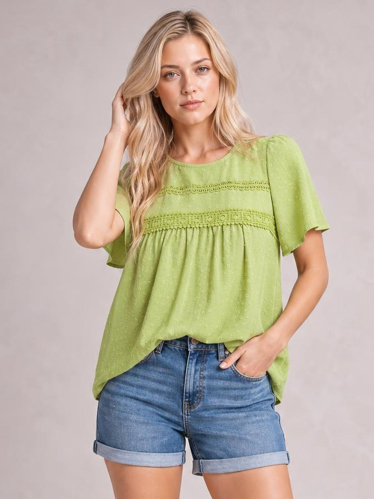 A model poses in a lime-green round-neck short-sleeve blouse with lace bands, ruched gathering, and a loose, flowing silhouette, one hand in a pocket.