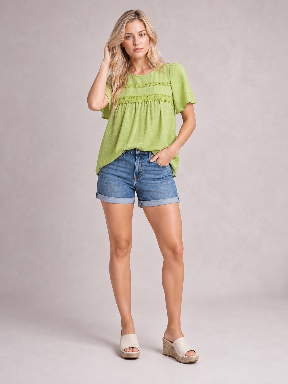 Model wearing a lime green round-neck short-sleeve blouse with lace trim, ruched detailing, eyelet texture, and a relaxed, flowing silhouette.