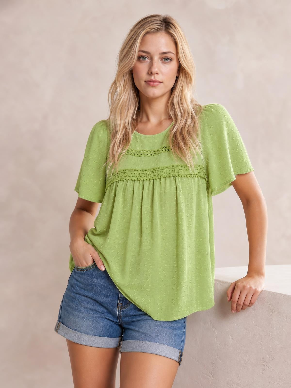 A model poses in a lime green round-neck blouse with short sleeves, lace detail and ruched gathering across the chest, creating a relaxed silhouette.