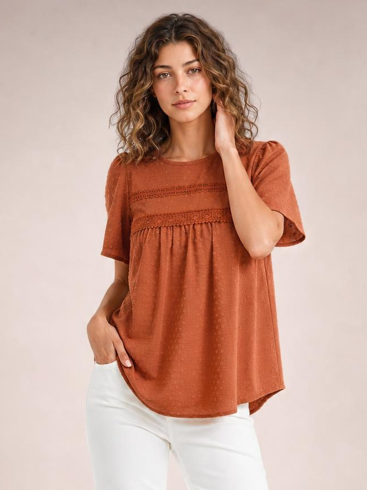 Model poses in a rust-brown round-neck blouse with short sleeves, lace detail, ruched trim, and a loose flowing silhouette.