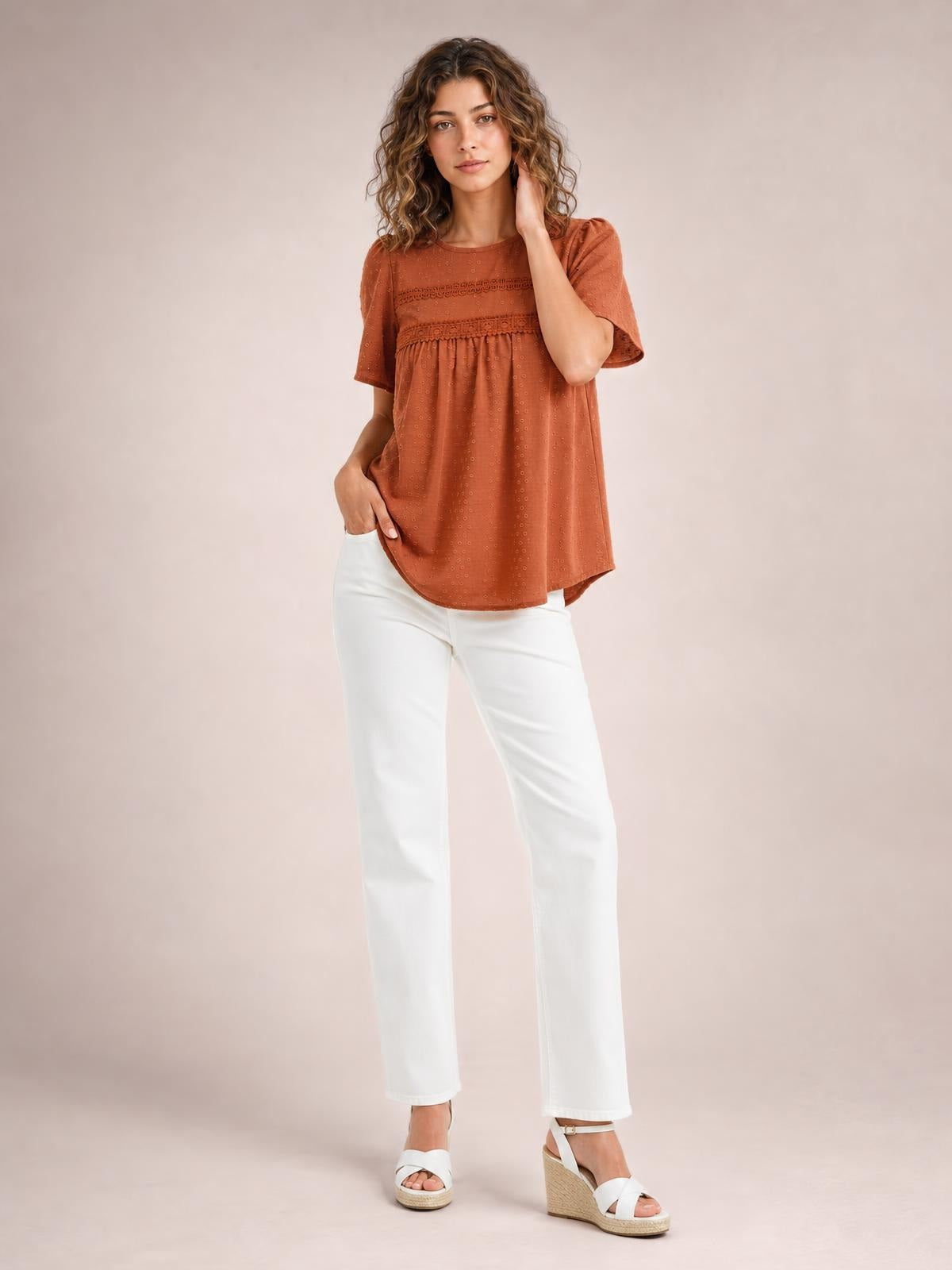 A model poses in a rust-colored lace detail round neck short sleeve blouse with ruched trim and a relaxed, flowing silhouette.