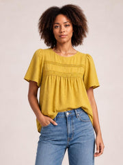Model wears a mustard yellow round-neck short-sleeve blouse with lace bands, ruched detailing, puffed shoulders, and a relaxed silhouette.