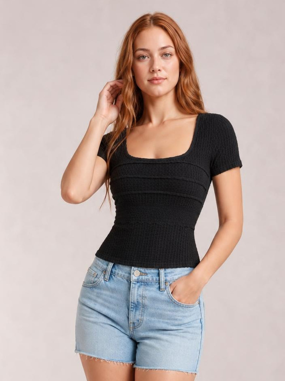 Model wearing a black square-neck short-sleeve T-shirt with a fitted silhouette, textured fabric, and horizontal seam details, paired with denim shorts.