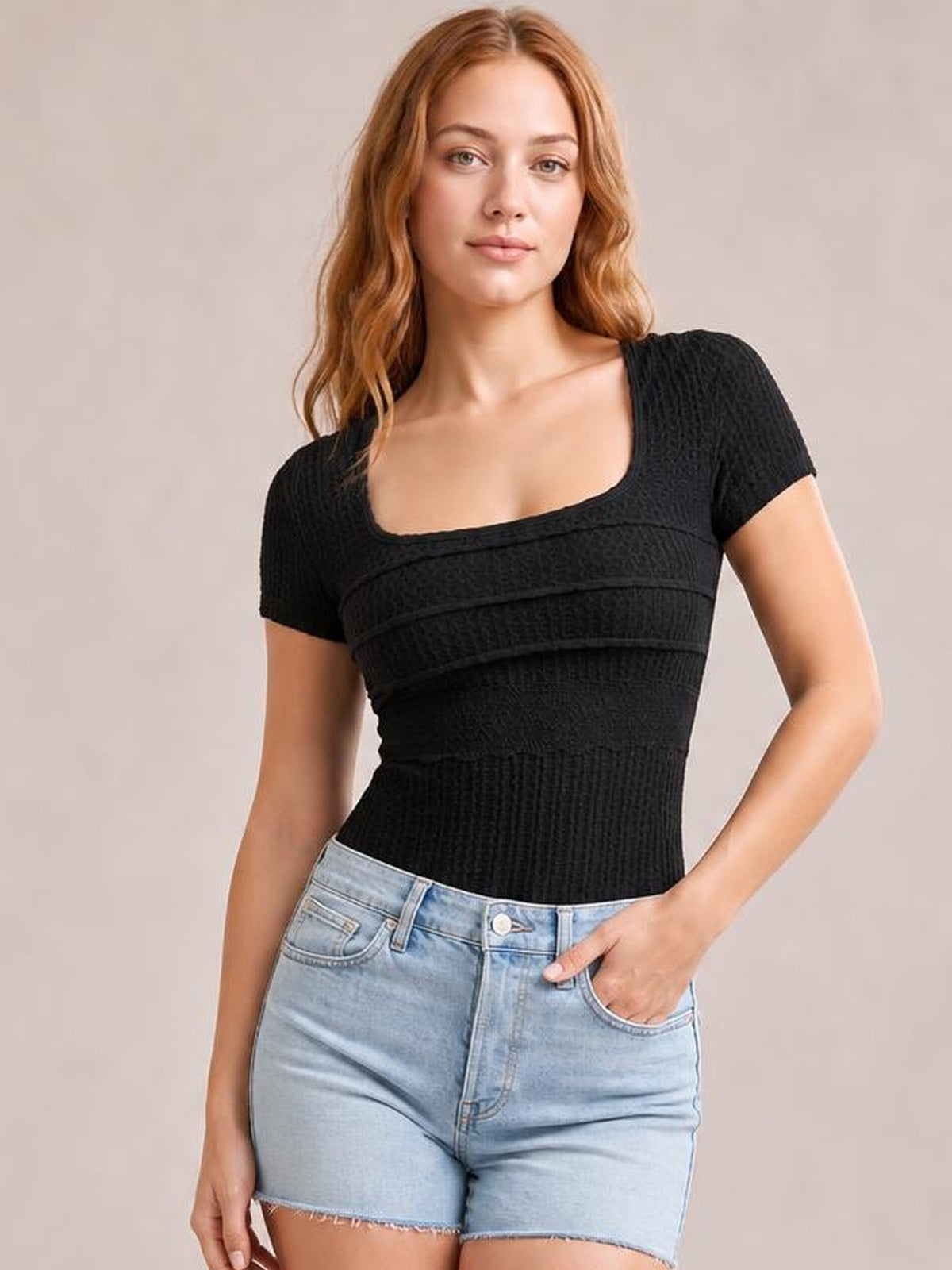 A model wears a fitted black lace-detail square-neck short-sleeve T-shirt with textured construction, posing with one hand in her denim shorts pocket.