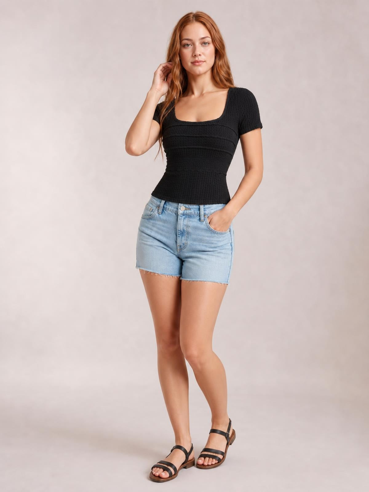 A model poses in a fitted black square-neck short-sleeve T-shirt with lace-textured construction, one hand touching her hair and the other in a pocket.