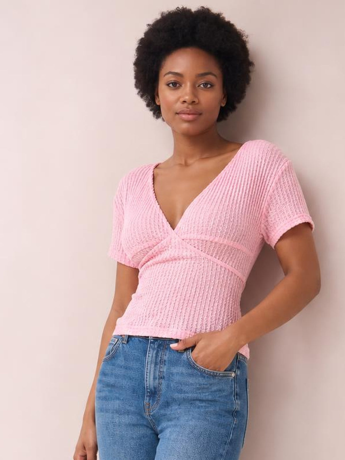 Model wearing a pink lace-detail short-sleeve T-shirt with a V-shaped neckline, tied waist detail, textured construction, and fitted silhouette.