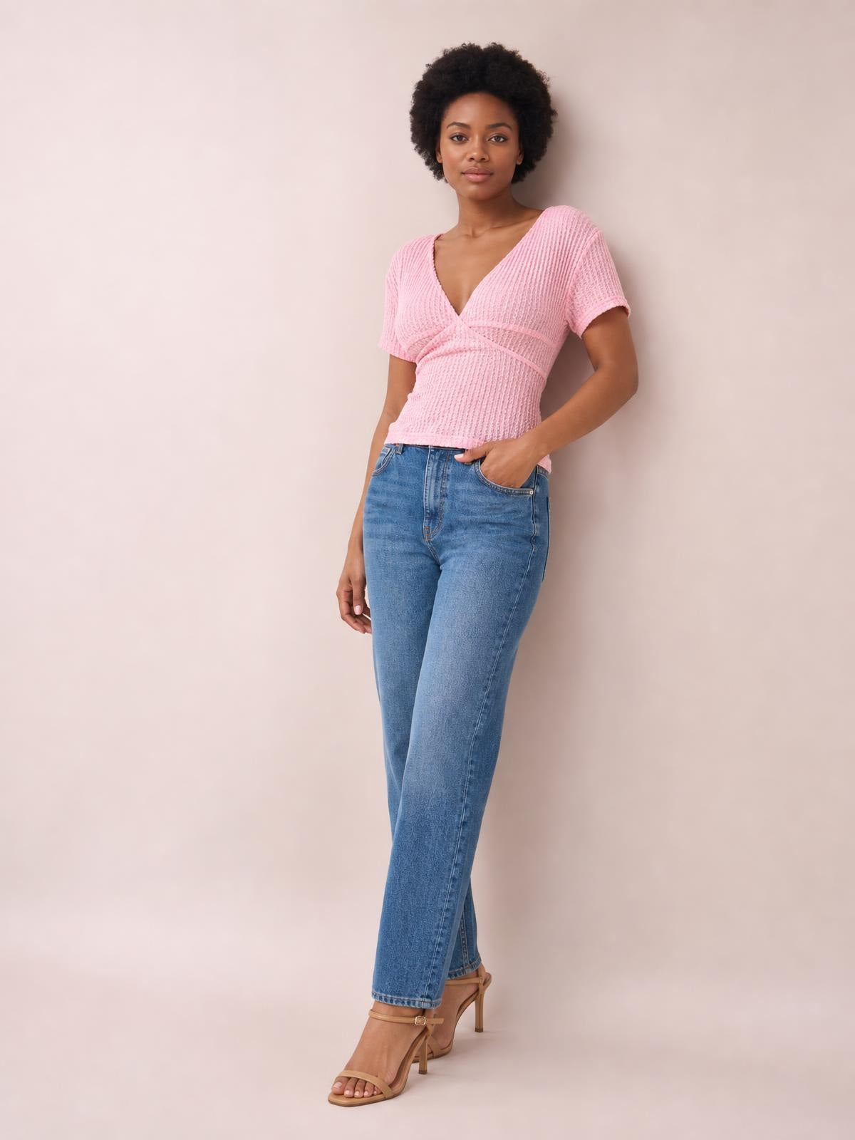 Model wears a pink short-sleeve T-shirt with lace detail, tied wrap front, fitted silhouette, and textured construction while posing with one hand in her pocket.