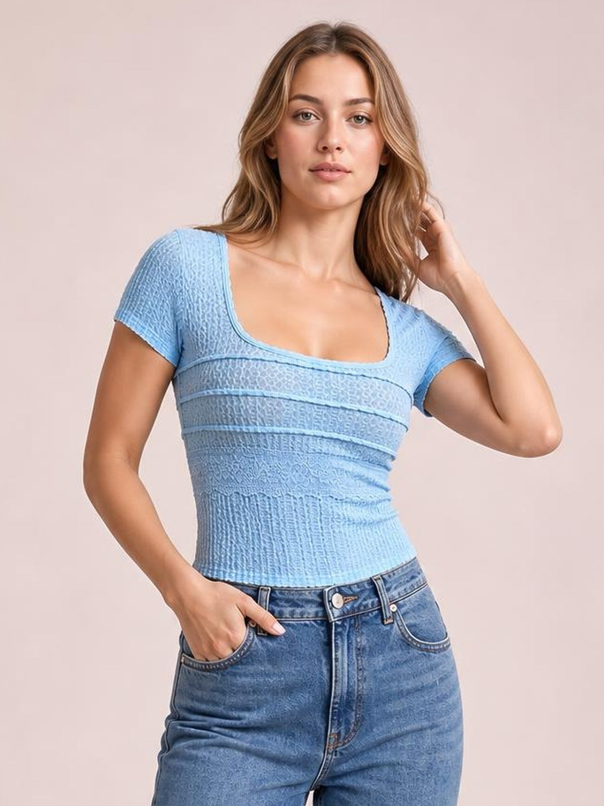 Model poses in a fitted light blue square-neck short-sleeve T-shirt with textured lace detail and horizontal seam construction, one hand in her jeans pocket.
