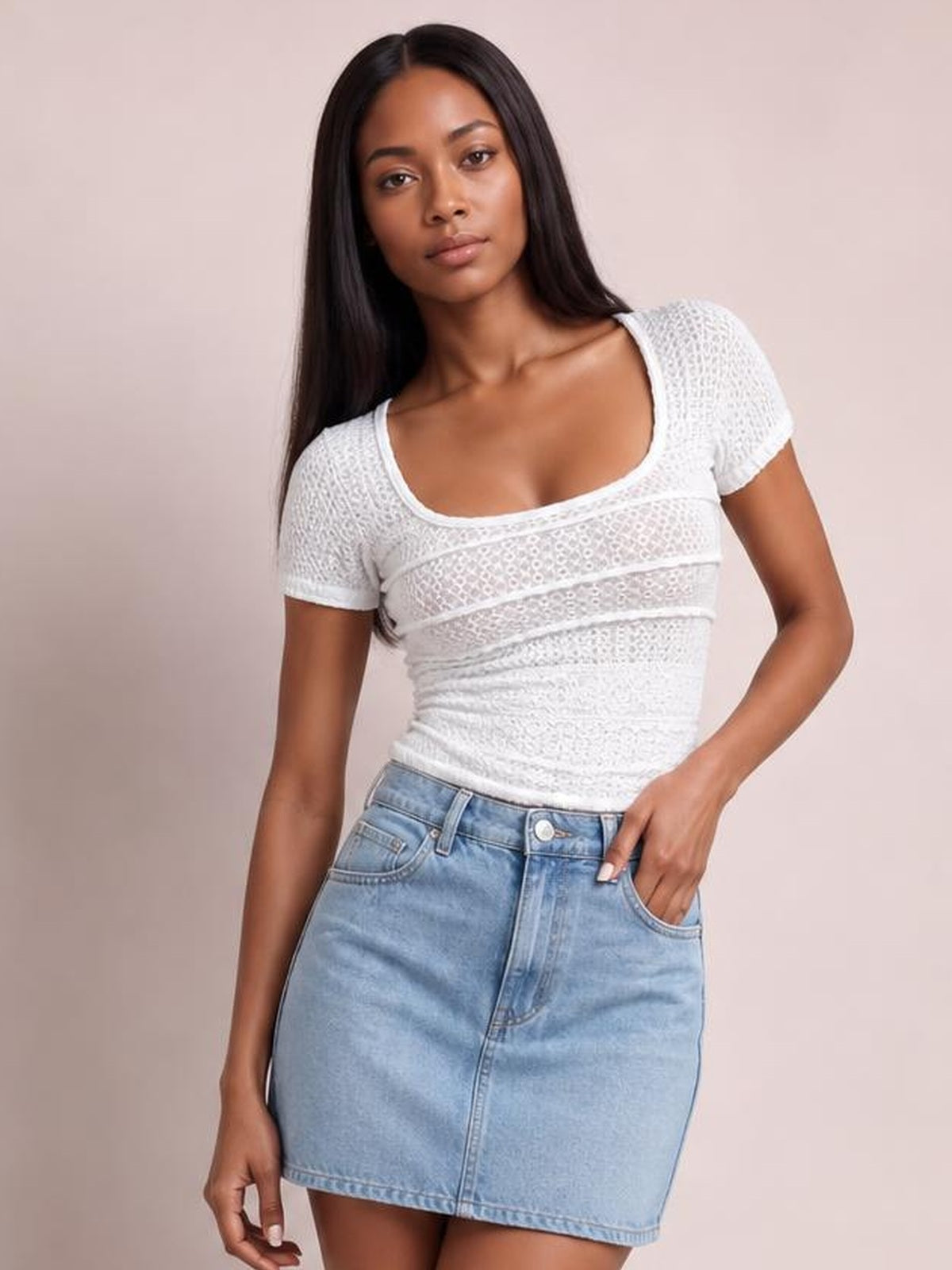 Model in a fitted white lace detail short sleeve T-shirt with a square neckline and horizontal panel construction, posing with one hand in her denim skirt pocket.