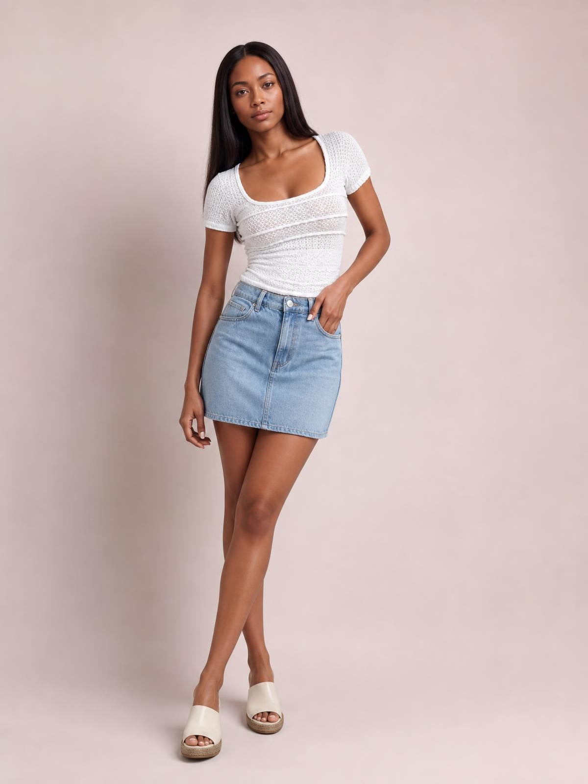 A model poses in a fitted white lace-detail square-neck short-sleeve T-shirt, styled with a light denim mini skirt and one hand in her pocket.
