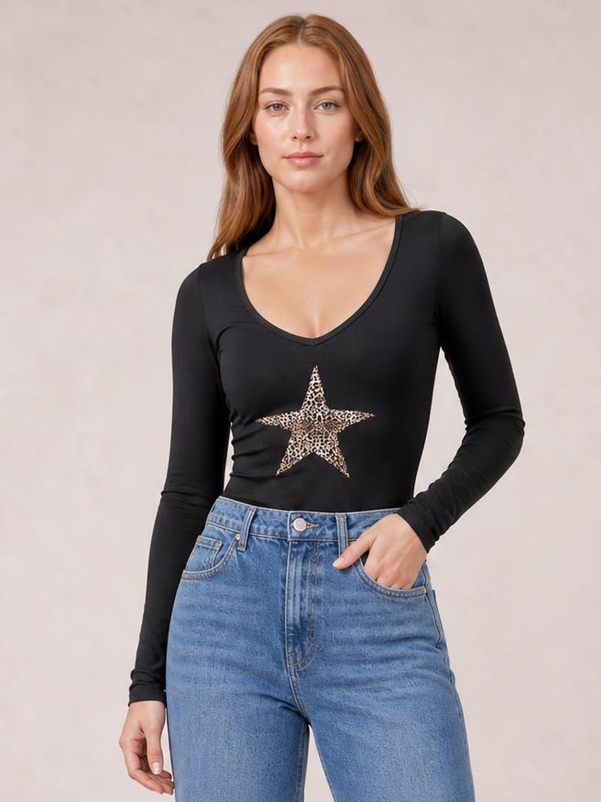 Model wearing a black Leopard Star long sleeve T-shirt with a scoop neckline, fitted silhouette, and leopard-print star graphic, posing with one hand in her jeans pocket.