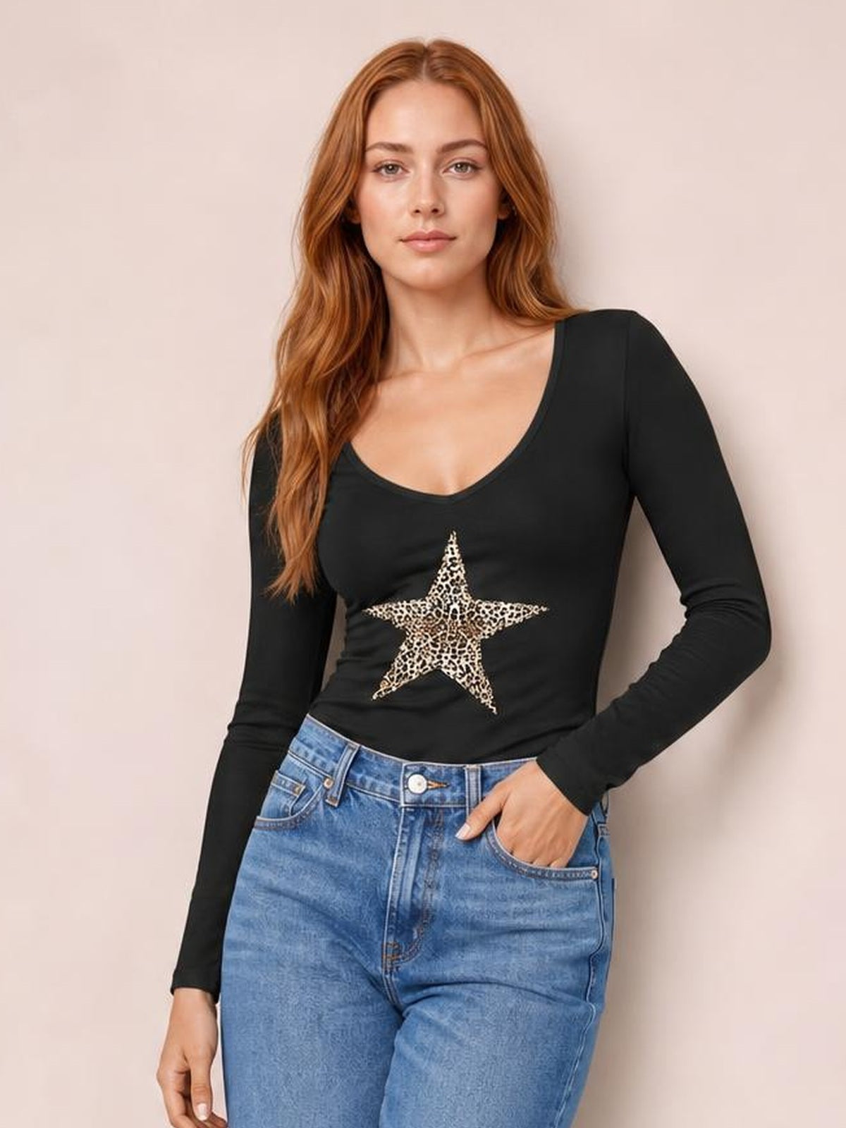 Model wears a black leopard star long sleeve T-shirt with a scoop neckline and fitted stretch silhouette, posing with one hand in her jeans pocket.