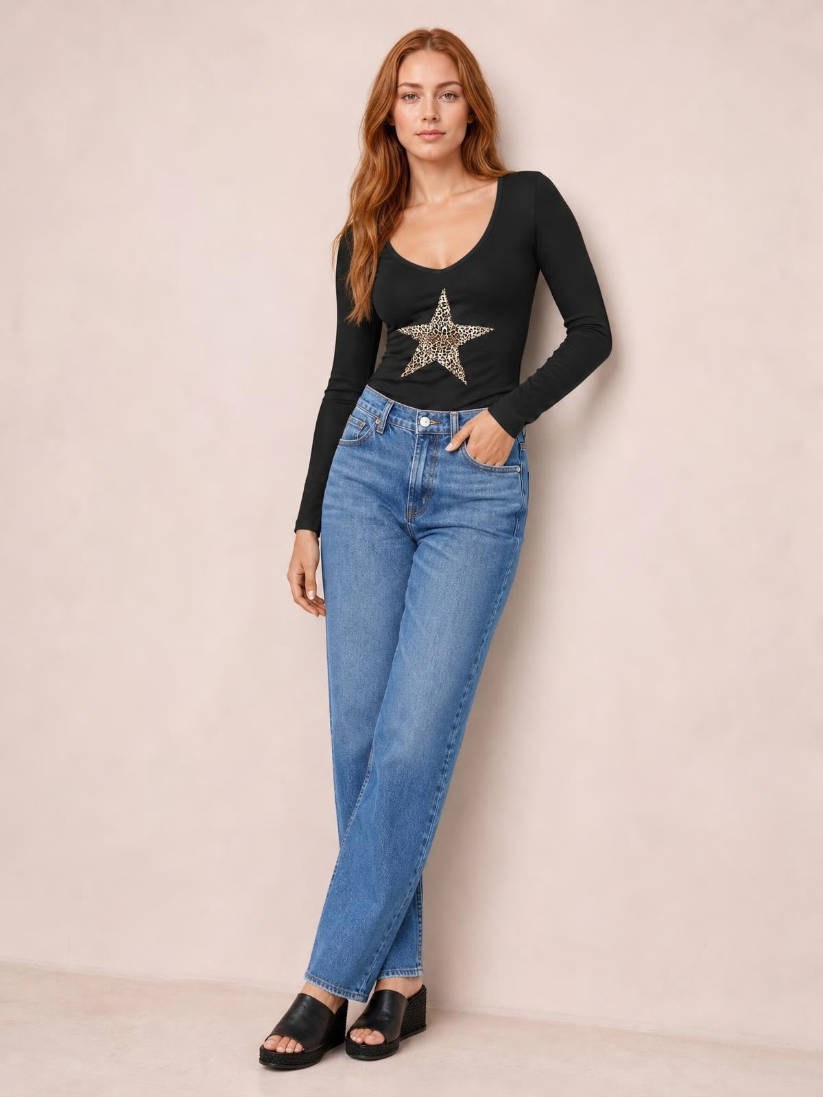 Model poses in a black Leopard Star long sleeve T-shirt with a scoop neckline, fitted silhouette, and leopard-print star graphic, one hand in her jeans pocket.