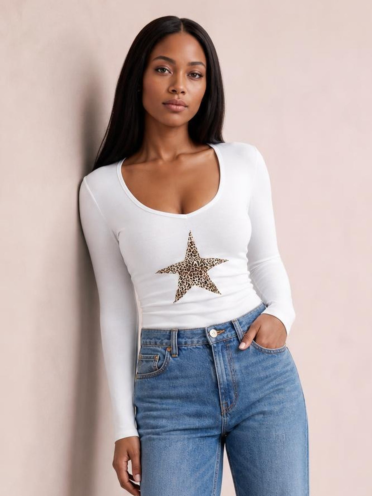 Model poses with one hand in her pocket wearing a fitted white leopard star long sleeve T-shirt with a scoop neckline and stretchy silhouette.