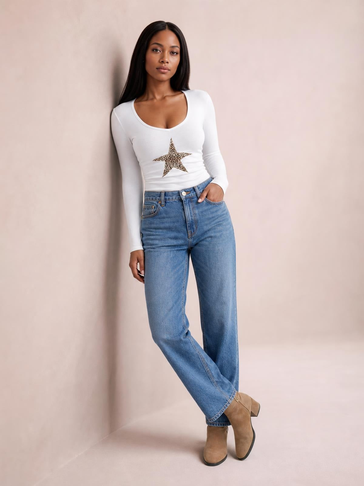 Model poses in a fitted white Leopard Star long sleeve T-shirt with a scoop neckline and leopard-print star graphic, paired with jeans.
