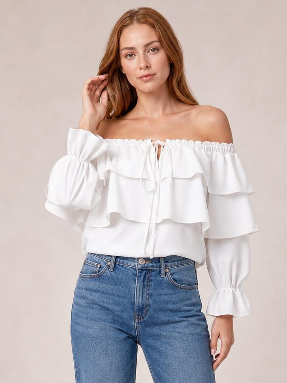 A model poses in a white off-shoulder blouse with layered ruffled flounce sleeves, gathered drawstring neckline, and a relaxed cropped silhouette.